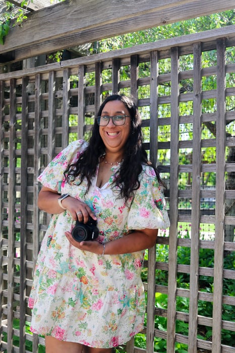 Ella Boozer standing against a fence holding a camera.